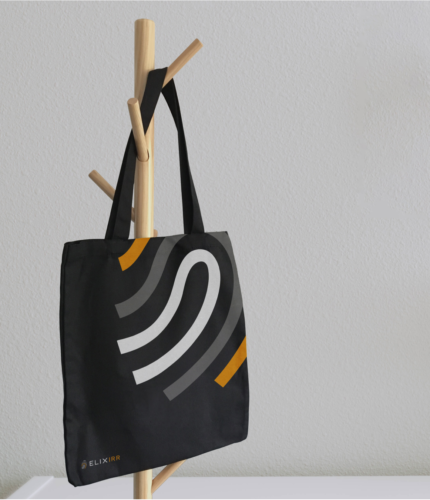 A black Elixrir branded tote bag handing on a wooden coat rack.