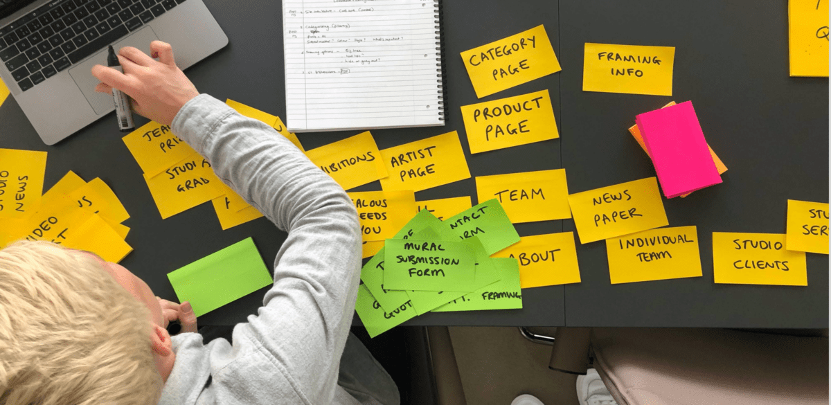 Woman sitting at a table full of post-it notes with a pen in her hand.
