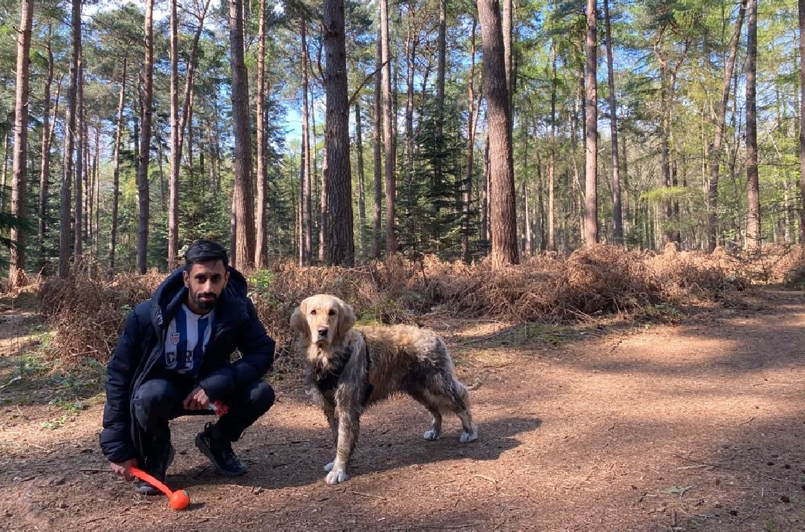 A man bending down next to a muddy dog in a forest.